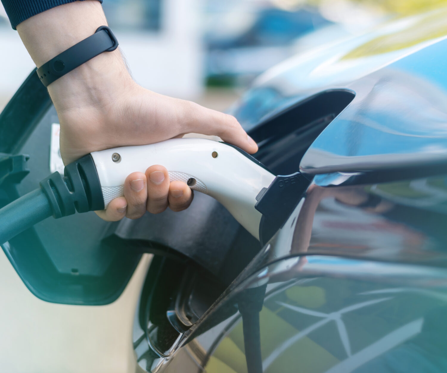 Man plugging in charger into an electric car at charge station